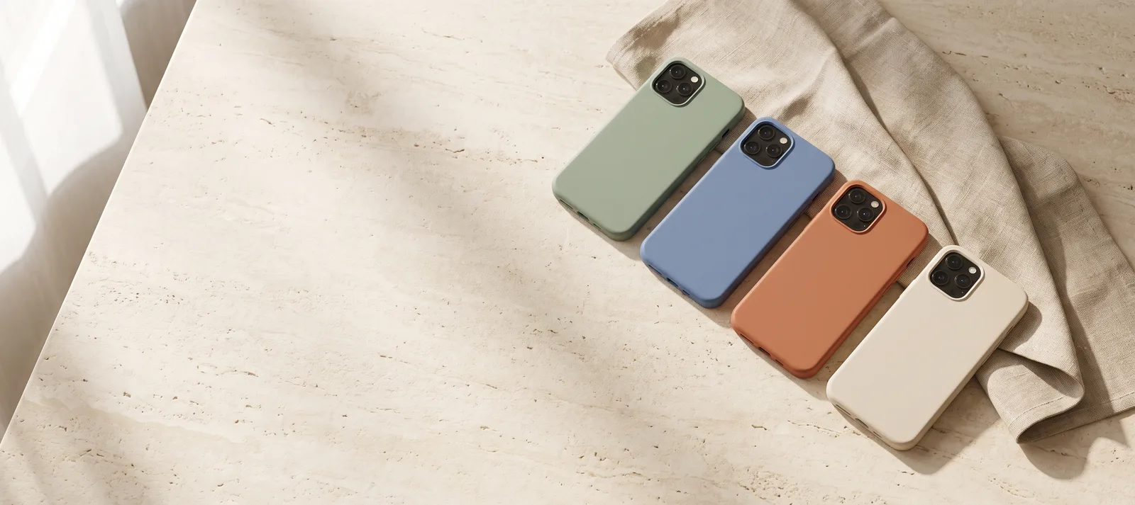 Four phones in sage, cornflower blue, terracotta and oat Huebury cases on pale stone